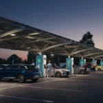 Several modern electric vehicles, including an SUV, charging at a busy, well-lit station at twilight.