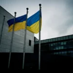 The European Parliament building in Brussels with the EU and Ukrainian flags flying together under an overcast sky.