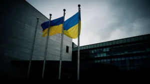 The European Parliament building in Brussels with the EU and Ukrainian flags flying together under an overcast sky.