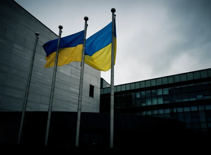 The European Parliament building in Brussels with the EU and Ukrainian flags flying together under an overcast sky.