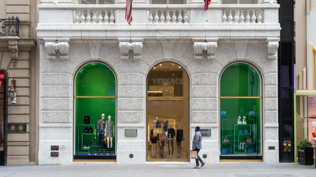 A Versace storefront with green-lit arched display windows on a marble facade