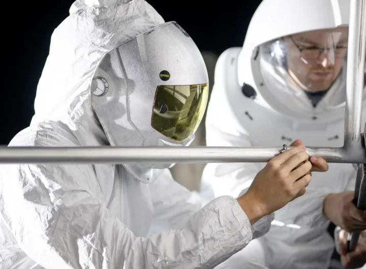 Two suited engineers work under harsh directional lighting during a NASA lunar surface lighting simulation for Artemis III