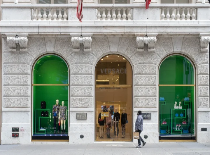 A Versace storefront with green-lit arched display windows on a marble facade